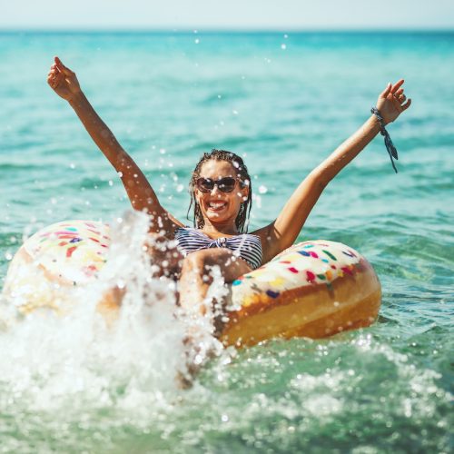 A beautiful young woman swims on inflatable ring donut, has fun at the sea water and enjoys on vacation.